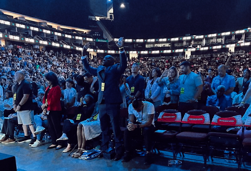 Attendees worship and pray during a powerful moment at the Life Surge Newark event, with a full arena visible in the background.