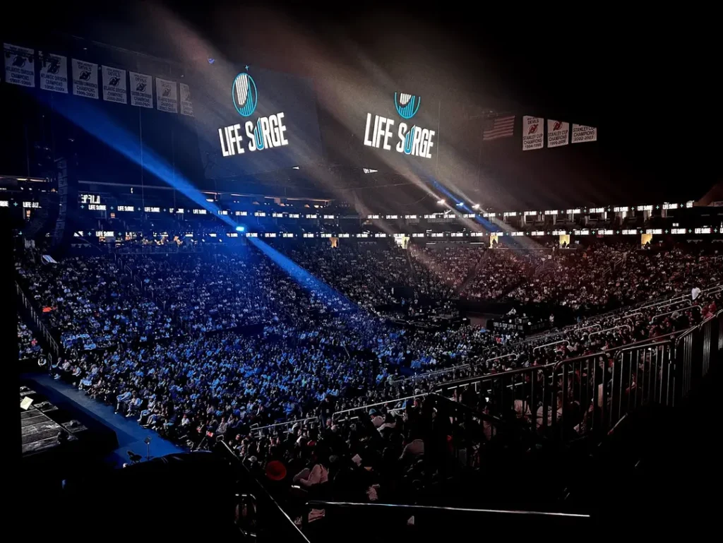 Packed arena at Life Surge Newark event with worship lighting and large Life Surge logo on screen at Prudential Center.
